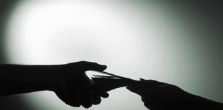 Billionaire-Backed FAKE Protests—$3 BILLION Secret Silhouette of hands exchanging money in dim light.