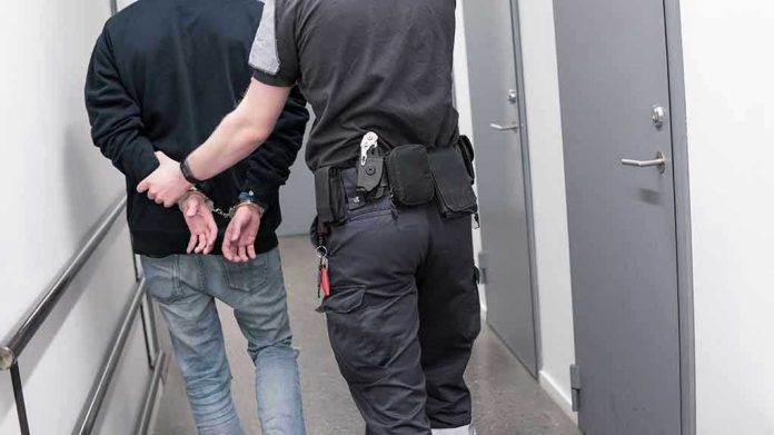 Officer escorting handcuffed person down hallway.