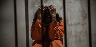 911 “Assault” Call Turns Unthinkable Person in orange jumpsuit sitting behind bars, handcuffed.