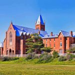 Large red brick building with turrets and green lawn.