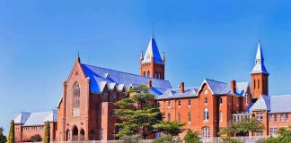 Large red brick building with turrets and green lawn.