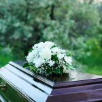 Coffin with white flowers outdoors in green surroundings.