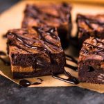 Chocolate brownies with drizzled chocolate on parchment paper.