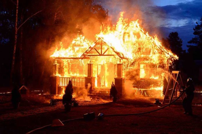 569622439 House engulfed in flames with firefighters present.