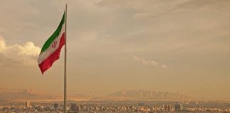 Iranian flag waving over a city skyline with mountains in the background