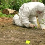 Forensic investigator in a protective suit collecting evidence from the ground