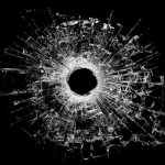 A bullet hole surrounded by shattered glass on a black background