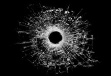 A bullet hole surrounded by shattered glass on a black background