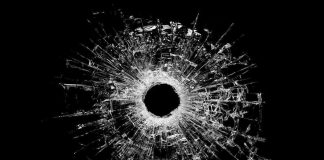 A bullet hole surrounded by shattered glass on a black background