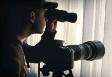 Person looking through binoculars beside a camera.