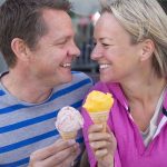 Couple smiling with ice cream cones outside bench
