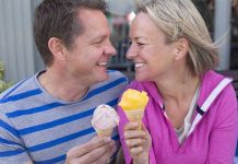 Couple smiling with ice cream cones outside bench