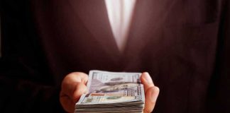 Diversity Plot EXPOSED — $17 Million Settlement Hand holding a stack of hundred-dollar bills.