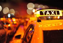 Close-up of a taxi sign illuminated at night with blurred city lights in the background