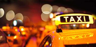 Close-up of a taxi sign illuminated at night with blurred city lights in the background