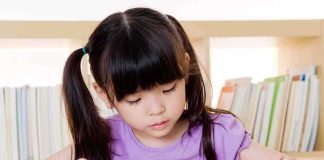 Library Director FIRED — Defied Order on Kids’ Books Young girl reading a book at a table with a bookshelf in the background