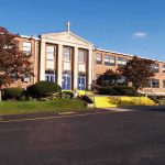 Exterior view of a brick school building with yellow steps and a cross on top