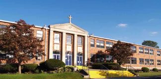 Exterior view of a brick school building with yellow steps and a cross on top