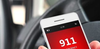 A smartphone displaying the emergency number 911 while held in a persons hand inside a car