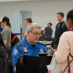Mandatory Screenings Expand Across U.S Airports! TSA agent checks passengers documents at airport security.