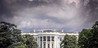 Trump Team SCRAMBLES – Situation Room Tapes LEAKED! White House front view with dark clouds above.