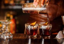 DISMEMBERED Bartender FOUNDER – Gruesome Murder Twist! Pouring cocktails into two glasses with lemon twists.