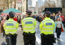 Terror Plot THWARTED: Boy, 14, Targets Mosques! Three police officers in high-visibility jackets stand facing a busy street
