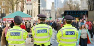 Terror Plot THWARTED: Boy, 14, Targets Mosques! Three police officers in high-visibility jackets stand facing a busy street