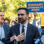 Mamdani SABOTAGES Historic 60-Year Tradition! A politician speaking at a rally with supporters holding signs