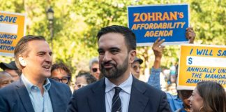 Mamdani SABOTAGES Historic 60-Year Tradition! A politician speaking at a rally with supporters holding signs