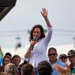 Woman speaking at outdoor event with raised hand.
