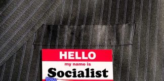 Socialist Movement SEIZING Properties Across the U.S Name tag on a pinstripe suit jacket pocket