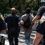 Man Arrested Outside Supreme Court With Guillotine Police escort a handcuffed man across a city street