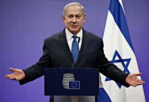 ICC Warrant Shadows Netanyahu’s UN Gamble man in suit speaking at a podium with Israeli flag