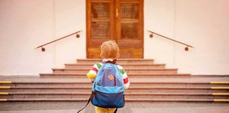 child with backpack walking toward school steps