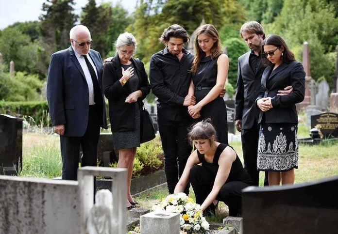 shutterstock_1230694315 Mourners gathered at a graveside placing flowers