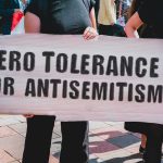Boycott Erupts Over Commie Mayor’s Kosher Dinner Protester holding a large sign at a rally