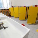 School bathroom with yellow stall doors and long sink
