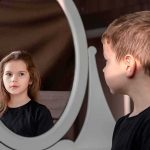 boy looking at reflection of a girl in an oval mirror