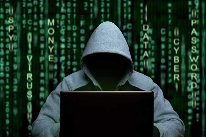 shutterstock_1708316974 Hooded figure using a laptop against green code backdrop