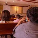 Talarico Creates NEW INCLUSIVE BIBLE people seated in church pews facing a cross