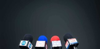 Four broadcast microphones on stands against a dark background