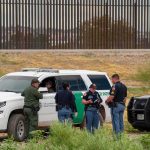 Routine ICE Stop Turns Deadly – Shocking Video! law enforcement officers confer beside patrol vehicles near a border fence