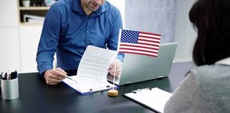 Two people at a desk reviewing documents with a small American flag by a laptop