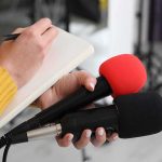 Conservative Activist ARRESTED Outside Airport! Journalist holding two microphones while writing in a notebook