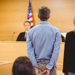 Defendant in handcuffs standing before a judge in a courtroom