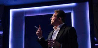 Grant Cardone EXPOSED In Class Action Lawsuit Man in suit giving a presentation on stage with blue backlighting
