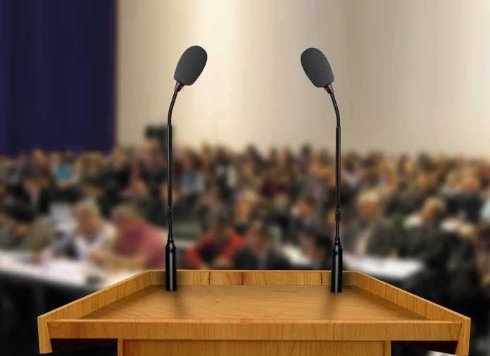 shutterstock_83211922 Podium with two microphones facing a blurred audience
