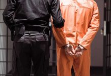 Trump to Execute Paraplegic Palestinian Prisoner in orange jumpsuit handcuffed with guard standing beside