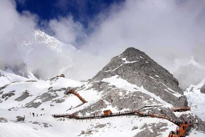 shutterstock_106809467 Snow-covered mountain with hiking trails and tourists under a cloudy sky